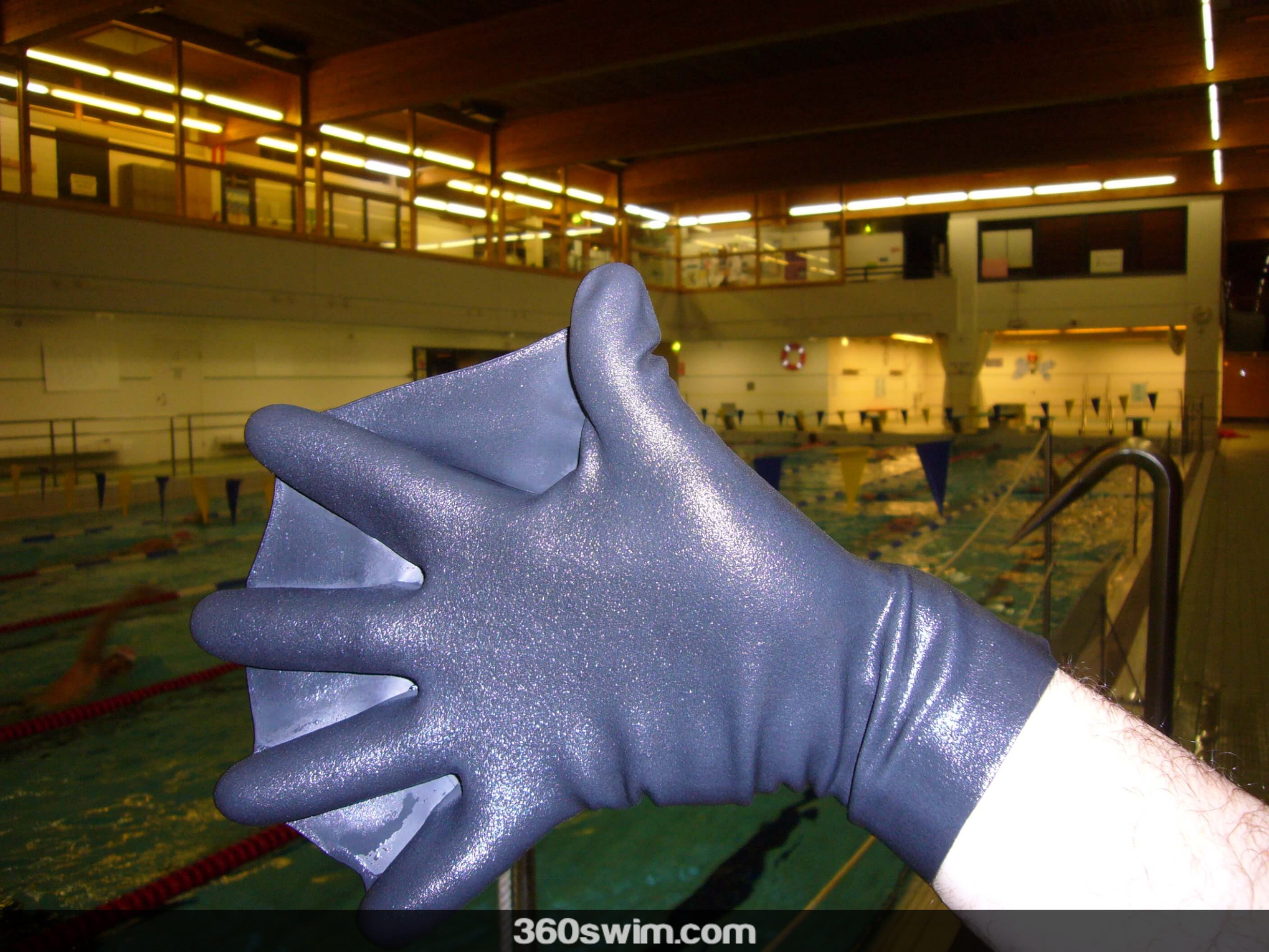 A person's hand wearing a black, webbed Darkfin swimming glove, with a swimming pool in the background.